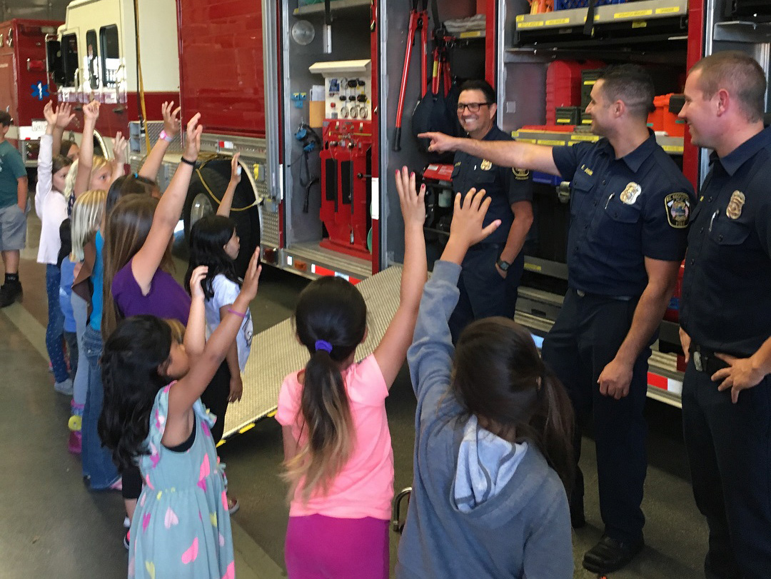 students raise their hands to ask questions at a fire station visit